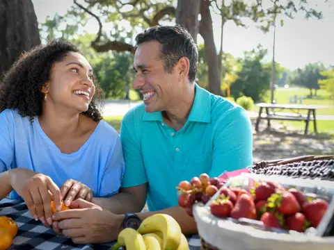 A smiling couple enjoying a picnic with fruit, showcasing a warm and engaging atmosphere.