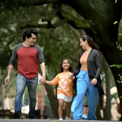 A family of three, consisting of a man, a woman, and a young girl, walking together in a park.