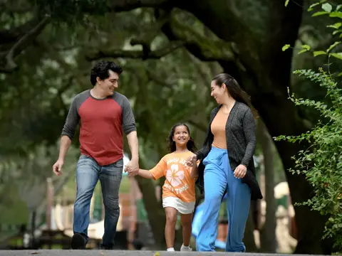 A family of three, consisting of a man, a woman, and a young girl, walking together in a park.