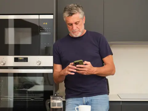 A middle-aged man using his phone in the kitchen.