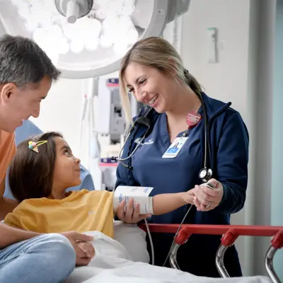 Father comforting his daughter while a nurse checks her blood pressure in an emergency care setting.