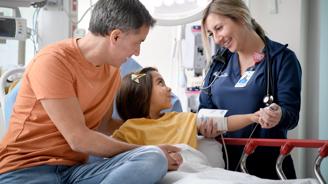 Father comforting his daughter while a nurse checks her blood pressure in an emergency care setting.