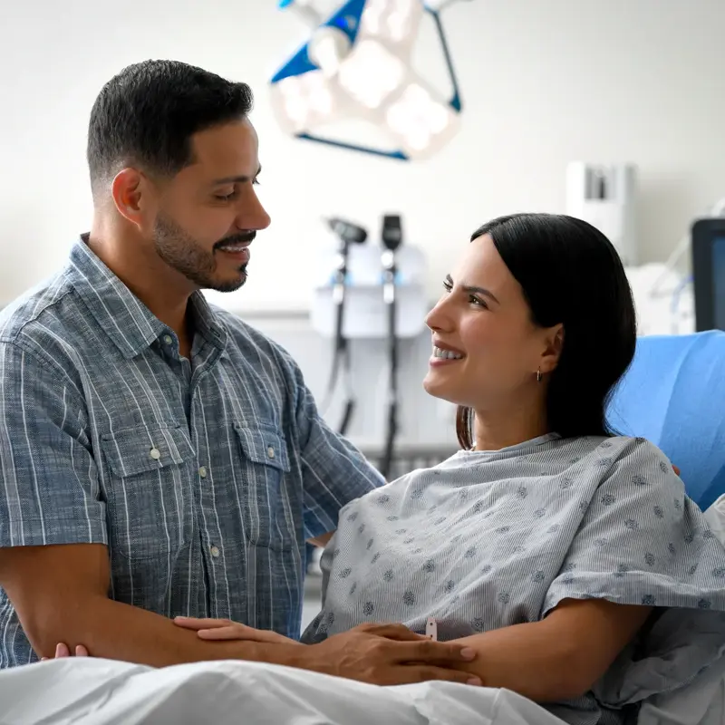 A man and woman in a hospital room, smiling and holding hands.
