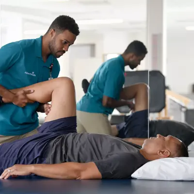 Physical therapist assisting a patient with leg exercises on a treatment table in a clinic.