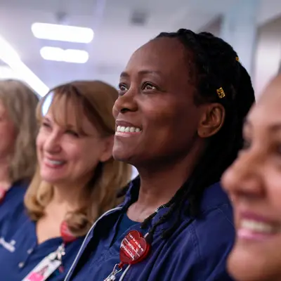Four smiling nurses in blue uniforms stand together in a hospital corridor, embodying warmth and care.