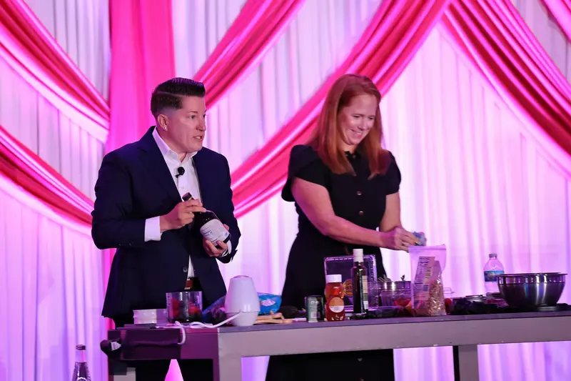 Two presenters demonstrating food preparation on stage during a women’s health event.