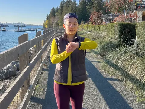 A woman check her watch while walking on a trail.