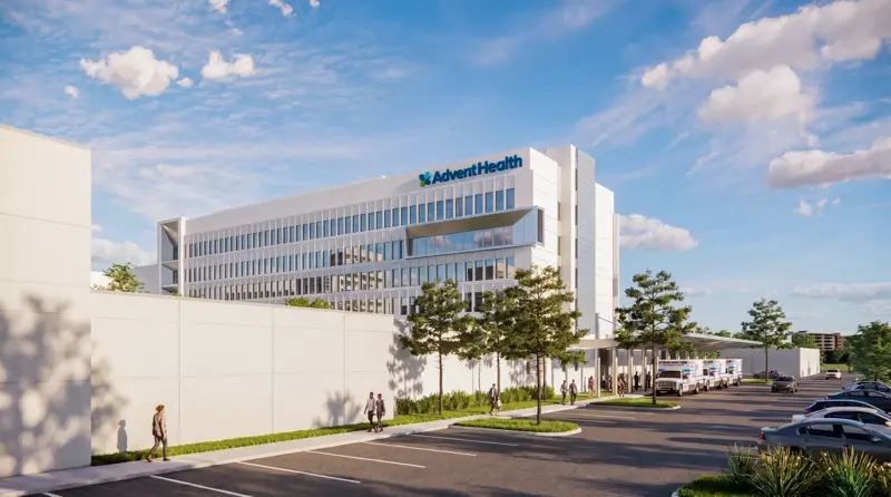 Exterior rendering of the modern AdventHealth Carrollwood Garden Tower expansion building with glass facade, featuring landscaped grounds, parking area, and people walking near the entrance under a blue sky with clouds