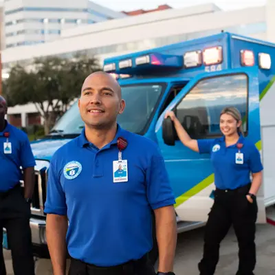Three AdventHealth employees in blue uniforms stand in front of an AdventHealth ambulance.