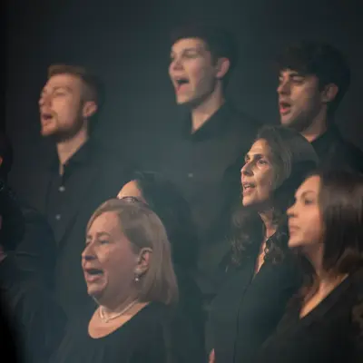 Choir members dressed in black sing together under soft stage lighting.