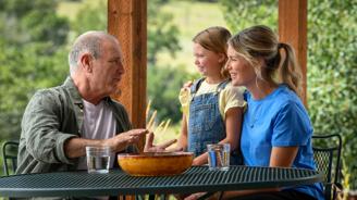An older man and two younger women sit at a table, smiling and talking.