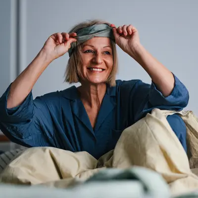 A middle-aged woman waking up in bed and smiling.