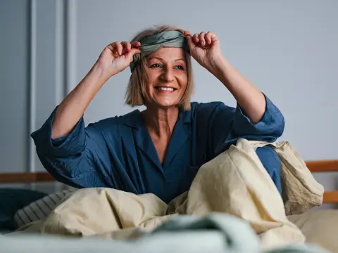 A middle-aged woman waking up in bed and smiling.
