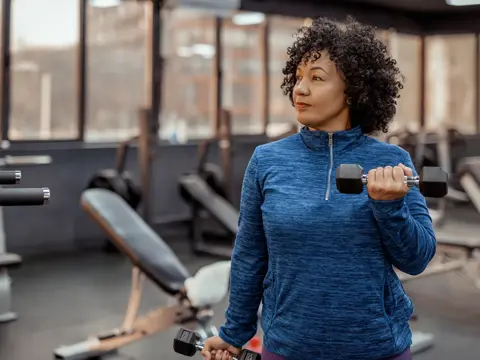 A middle-aged woman lifting dumbbells at the gym.