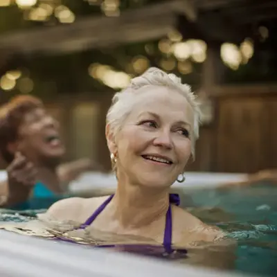 Two women laugh while soaking in an outdoor spa