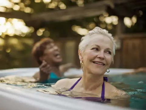 Two women laugh while soaking in an outdoor spa