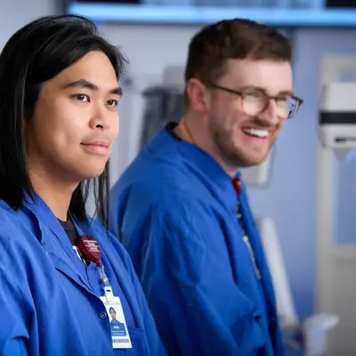 Two healthcare professionals in blue scrubs standing side by side in a hospital setting