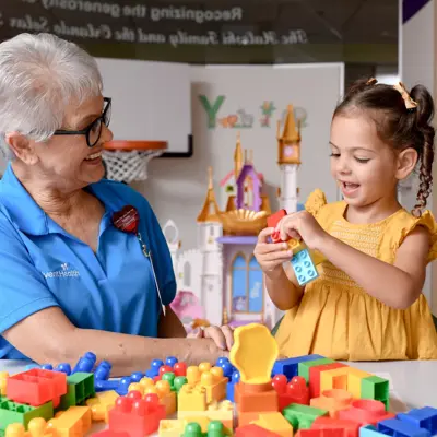 An older woman and a young girl are playing with colorful building blocks at a table.