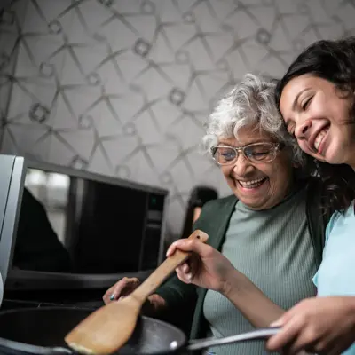 Two women cooking together in a kitchen, sharing a laugh and a hug.