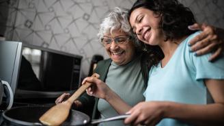 Two women cooking together in a kitchen, sharing a laugh and a hug.