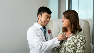 Physician using a stethoscope to examine a smiling patient in a medical office.