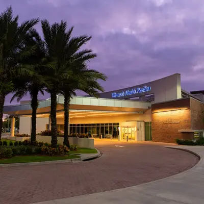 Evening view of the Women's Health Pavilion entrance with palm trees and a lit pathway.