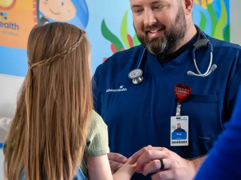 A smiling nurse holds the hand of a young girl in a pediatric clinic.