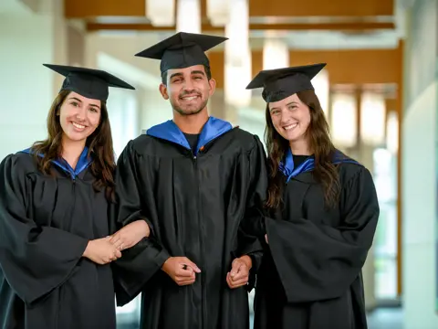 Three graduates in black gowns and caps, smiling and posing for a photo.