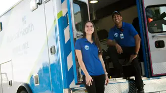 A smiling woman stands next to an AdventHealth ambulance with a smiling man inside.