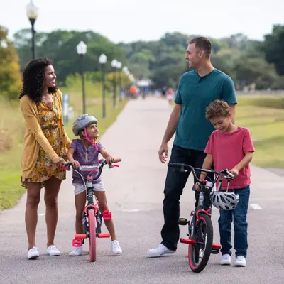 Family of four with two children on bikes, smiling and enjoying a park pathway.