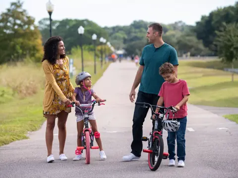 Family of four with two children on bikes, smiling and enjoying a park pathway.