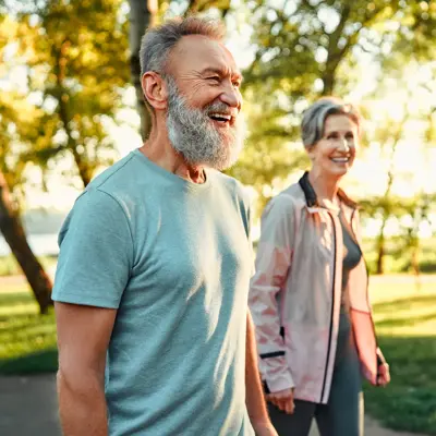 Grey haired caucasian man with beautiful wife strolling at summer park and smiling cheerfully. 