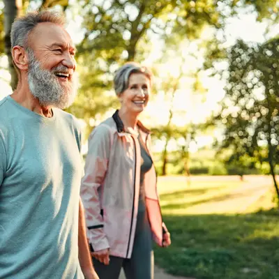 Grey haired caucasian man with beautiful wife strolling at summer park and smiling cheerfully. 