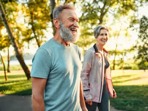 Grey haired caucasian man with beautiful wife strolling at summer park and smiling cheerfully. 