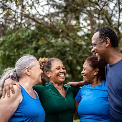 Four older adults in athletic clothing smiling together with their arms around one another outdoors.