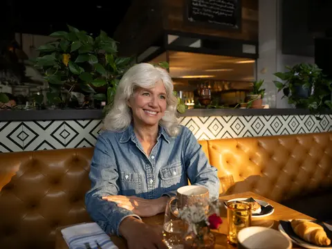 Smiling woman sitting at a table in a restaurant with food and drinks.