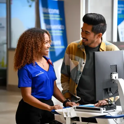 A smiling AdventHealth employee assists a patient at a computer in a welcoming healthcare setting.