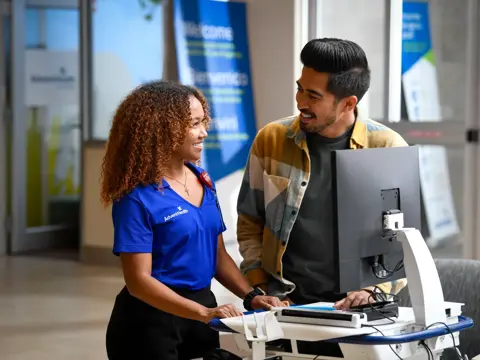 A smiling AdventHealth employee assists a patient at a computer in a welcoming healthcare setting.