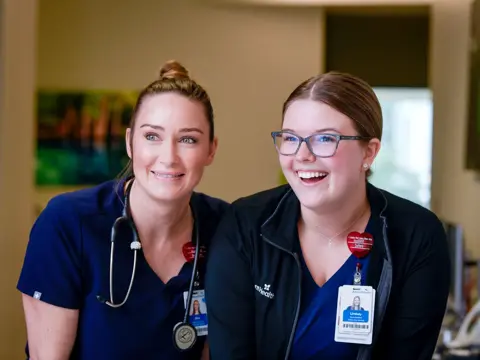 Two smiling AdventHealth employees, one with a stethoscope, stand together in a medical office.
