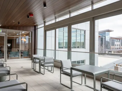 Modern hospital healing terrace with floor-to-ceiling windows, contemporary seating furniture, and views of adjacent medical buildings under natural daylight