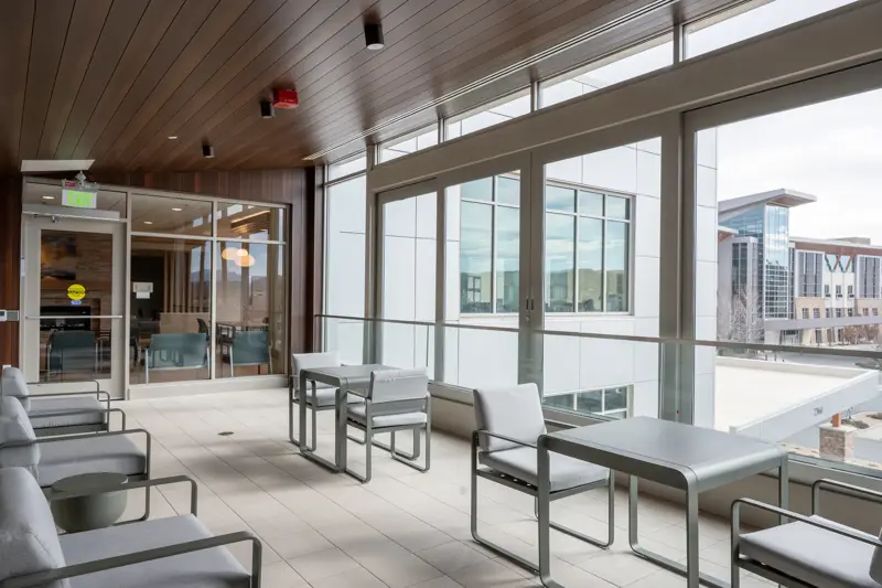 Modern hospital healing terrace with floor-to-ceiling windows, contemporary seating furniture, and views of adjacent medical buildings under natural daylight
