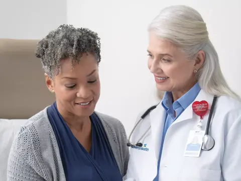 A smiling doctor and patient look at a tablet together in a medical office.