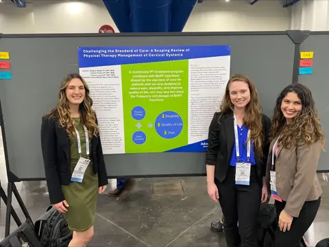 Three people stand by a poster on physical therapy management of cervical dystonia.