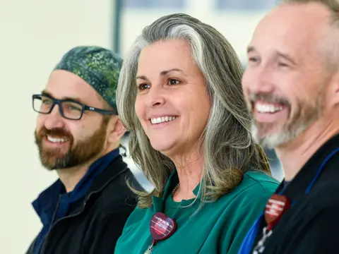 Smiling health care team members in medical scrubs standing together in a bright clinical setting, with a female team member in teal scrubs prominently featured in the center