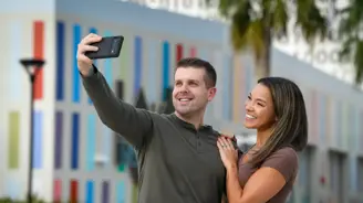 A smiling man and woman taking a selfie in front of a colorful building.