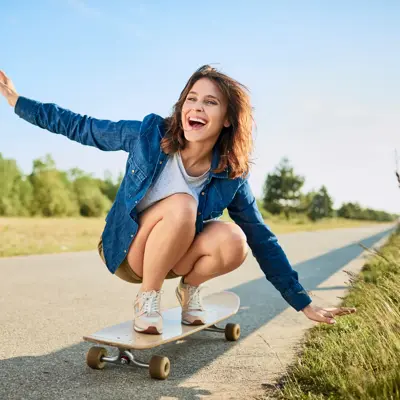 Ecstatic woman riding longboard on road in the countryside.