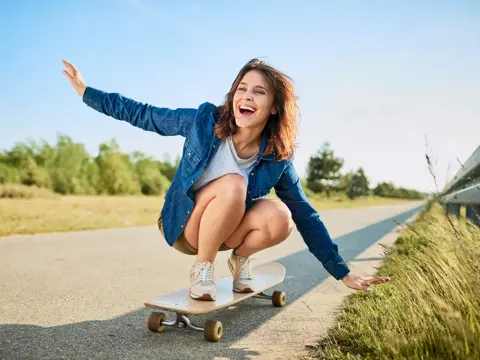 Ecstatic woman riding longboard on road in the countryside.