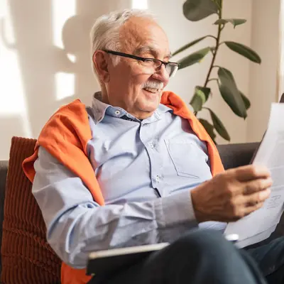 An older man sitting on a couch reading some papers.