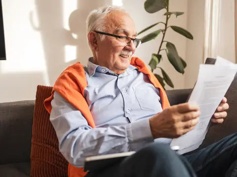 An older man sitting on a couch reading some papers.