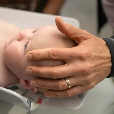 A newborn baby in a diaper is being held by a person's hands in a hospital setting.